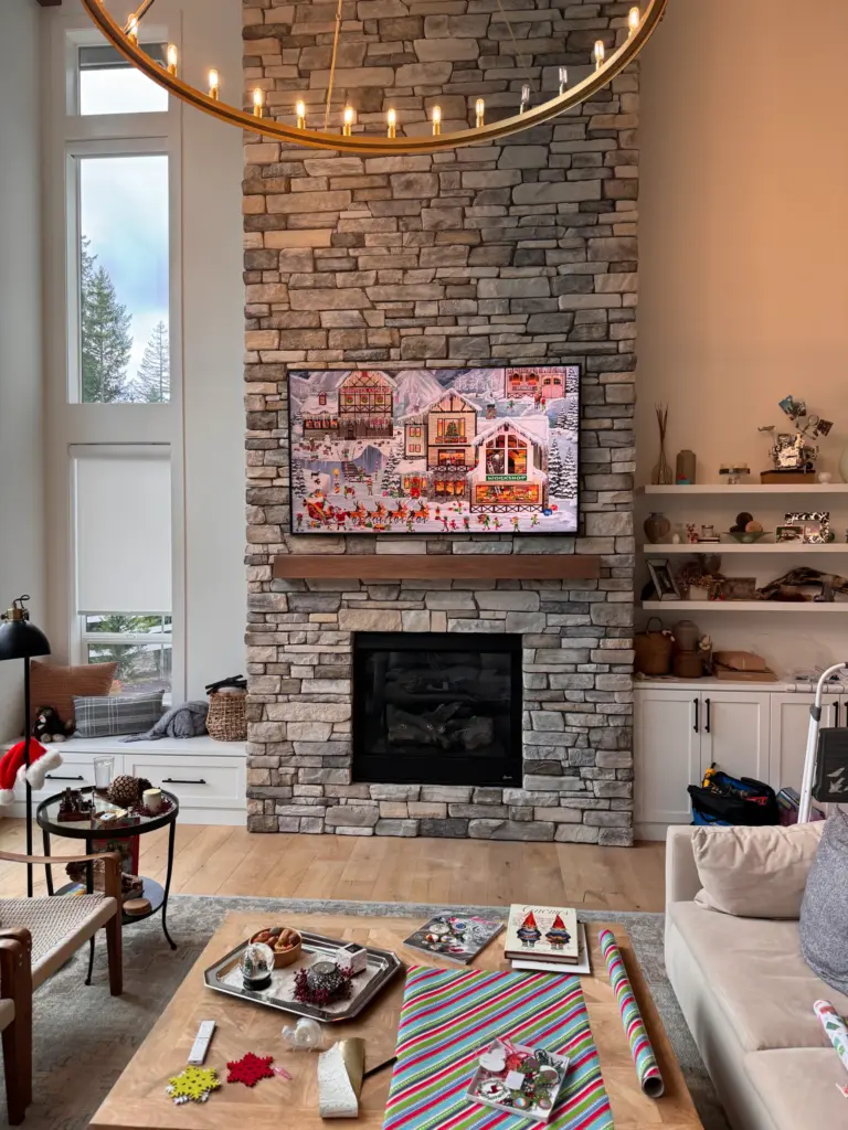 Samsung Frame TV mounted above a stone fireplace in a modern living room with tall windows and custom built in shelving.