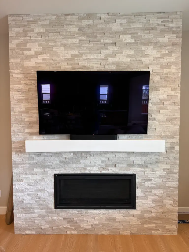 TV mounted above a modern fireplace with stacked stone surround and soundbar installation in Lacey Washington.