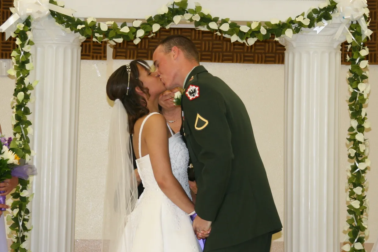 Alex and Jenae sharing a kiss during their wedding ceremony with Alex wearing his Army dress uniform.