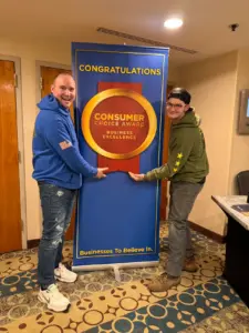 Alex Zehm and Josh Norcott posing with Consumer Choice Award banner celebrating business excellence in Seattle Washington